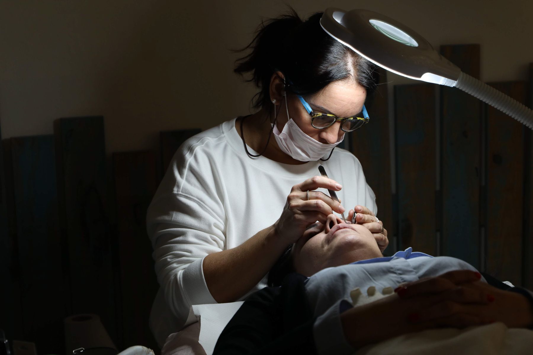 Beauty therapist applying eyelash extensions under a lamp